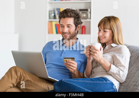 Mitte erwachsenes paar Einkaufen mit Laptop und Kreditkarte in modernen Wohnung. E-Commerce Stockfoto