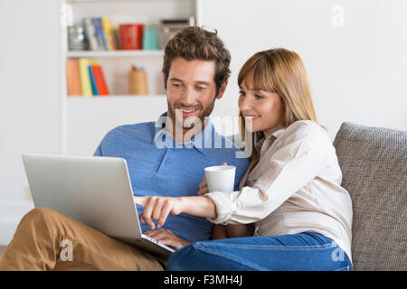 Junges Paar mit Laptop im Internet surfen. Moderne Ferienwohnung im Hintergrund Stockfoto