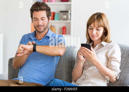Digitale Geek zu zweit am Hone auf Couch mit Smartwatch En Handy Stockfoto