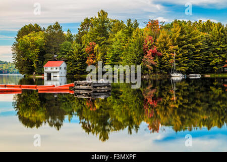 Ein Glas wie Spiegelung ein Bootshaus, Segelboot und schwimmt auf Mary Lake im Herbst. Stockfoto