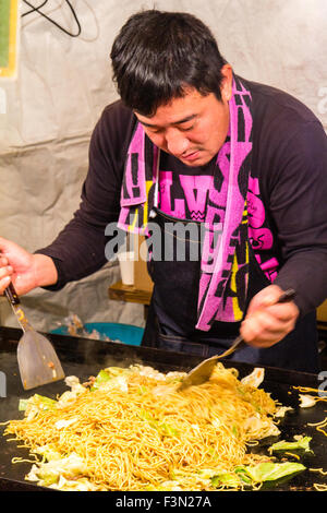 Japan Festival Food. Nacht. Yakisoba ausgeht, Mann kochen und mixen gebratene Nudeln mit zwei spezielle Nudeln schneiden. Stockfoto