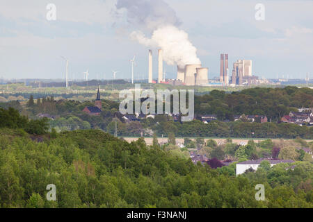 Blick von einer Halde über ländliche Landschaft zu einem fernen dampfenden Kohle befeuerten Kraftwerk umgeben von Windkraftanlagen. Stockfoto