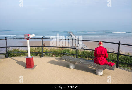 Rückansicht der Frau im roten Mantel mit Blick über Saltburn Pier und Strand von oben Promenade. Saltburn am Meer, North Yorkshire, Großbritannien Stockfoto