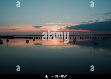 Sonnenuntergang auf der Hayling Billy-Brücke. Blick über Langstone Hafen in Richtung der untergehenden Sonne hinter Portsmouth auf einen ruhigen Abend. Stockfoto