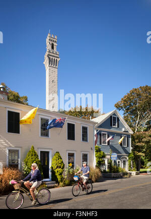 Paar Biken vor Gabriels Bed And Breakfast mit Pilgrim Monument im Hintergrund, Provincetown, Massachusetts, USA Stockfoto