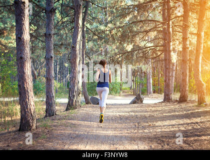 Junge Frau auf einer Landstraße bei Sonnenuntergang im herbstlichen Wald ausgeführt. Lifestyle-Sport-Hintergrund Stockfoto