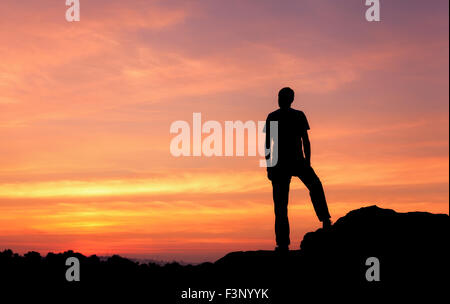 Silhouette eines Mannes mit angehoben bis Armen an den wunderschönen Sonnenuntergang auf dem Berg. Hintergrund Stockfoto