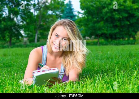 Blondine posiert in einem Park liegen auf den Rasen und Notizen in einem Notizbuch Stockfoto