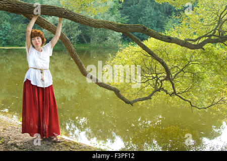 Europäische Frau mit braunen Haaren im Park steht in der Nähe von See mit großen Zweig der Weide. Stockfoto