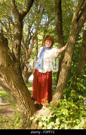 Europäerin mit Schuss braunen Haaren im roten Rock und weißer Bluse zu Fuß im Park stehen in der Nähe von schönen Weiden. Stockfoto