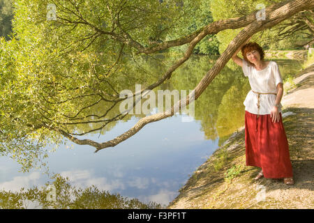 Europäerin mit Schuss braunen Haaren im roten Rock und weißer Bluse zu Fuß im Park in der Nähe von See. Stockfoto