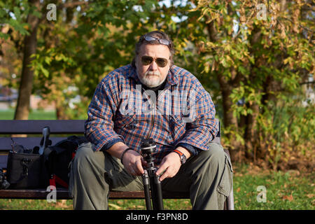 Man sitzt auf der Bank und hält Stativ im Herbst Stockfoto