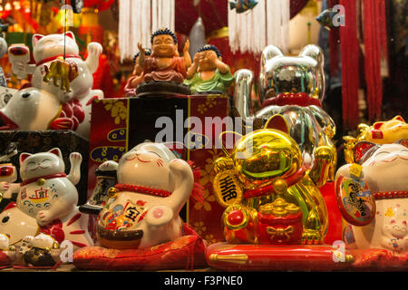 Verschiedene Größen von Maneki Neko (japanische verlockende Katzen) im Abendlicht auf rotem Grund. Stockfoto