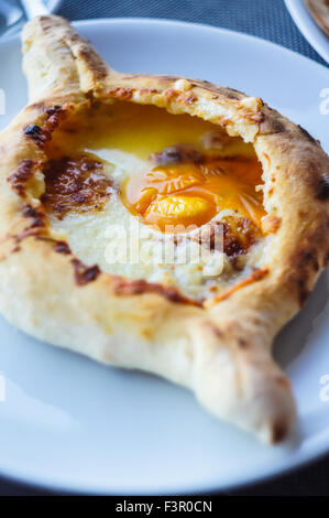 Ajarian oder Adjaruli Khachapuri, gefüllt mit Käse und garniert mit einem rohen Ei und Butter - traditionelles Gericht der georgischen Küche Stockfoto