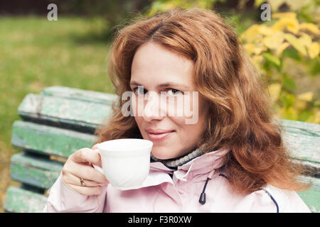 Junge Erwachsene kaukasischen Frau trinkt Kaffee im herbstlichen park Stockfoto