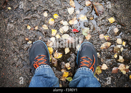 Männliche Füße in Sportschuhe stehen auf schmutzigen Straße mit gelben fallende Blätter im Herbst park Stockfoto