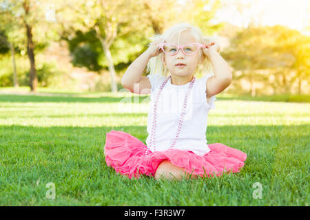 Niedliche kleine Mädchen Dress In The Grass mit rosa Brille und Perlenkette spielen. Stockfoto