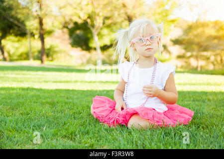 Niedliche kleine Mädchen Dress In The Grass mit rosa Brille und Perlenkette spielen. Stockfoto