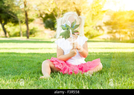 Niedliche kleine Mädchen sitzen Gras weht auf Windrad Spielzeug. Stockfoto