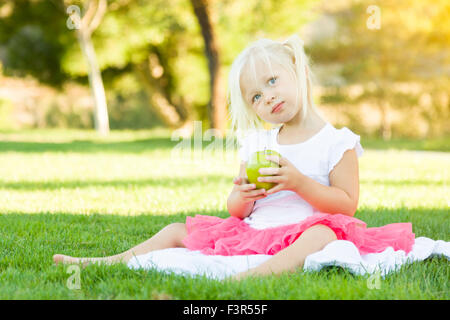 Niedliche kleine Mädchen sitzen im Rasen gesunde Apfel essen. Stockfoto