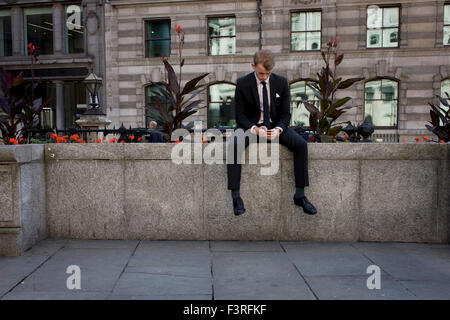 Ein junger Arbeiter der Stadt wartet auf einen Freund auf Bank-Dreieck in der City of London, der Hauptstadt Finanzviertel und ältesten Viertel. Stockfoto