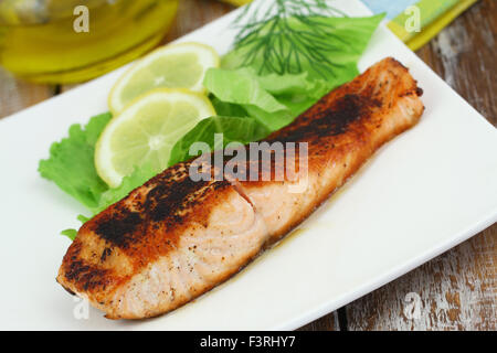 Gegrilltes Lachssteak mit grünem Salat und Zitrone auf weißen Teller Stockfoto