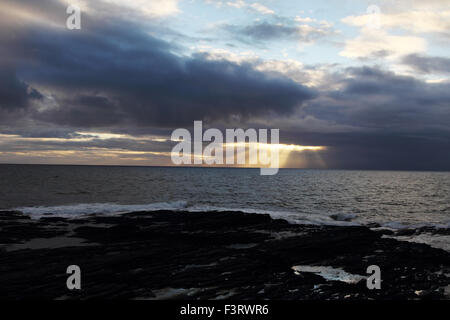 Die untergehende Sonne durch die Wolken über dem Atlantik mit dunklen Felsenküste Stockfoto