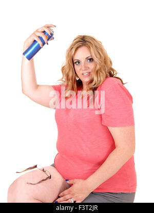 Ein schönes Plus Größe Frau in kurzen Hosen auf einem Stuhl sitzt und ihr Haar Haarspray Aufsprühen Feind weißen Hintergrund isoliert. Stockfoto