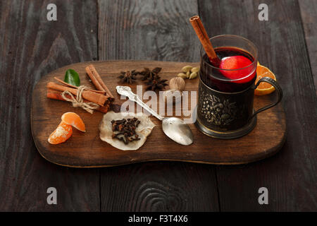 Glas Glühwein (Punch) in Glas-Halter über dunklen Holztisch auf Holzteller mit Gewürzen serviert. Stockfoto