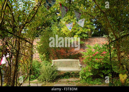 Eine Holzbank ist eingerahmt von einem Bogen aus Weide und verziert mit Girlanden in einem ummauerten Garten, Spätsommer, England, UK Stockfoto