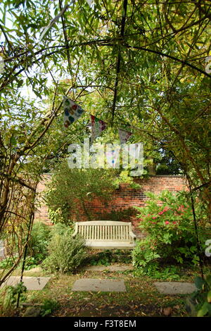 Eine Holzbank ist eingerahmt von einem Bogen aus Weide und verziert mit Girlanden in einem ummauerten Garten, Spätsommer, England, UK Stockfoto