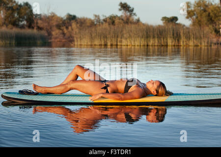 Eine junge Frau, die ein entspannendes Nickerchen auf einem Paddle Board während des Urlaubs an einem kleinen See in Nord-Kalifornien. Stockfoto