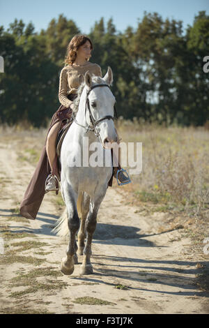 Schöne Mädchen reiten auf dem weißen Pferd in einem Feld Stockfoto