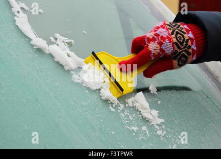 Hand der Frau in Eis und Schnee vom Auto Windschutzscheibe kratzen Handschuh Stockfoto