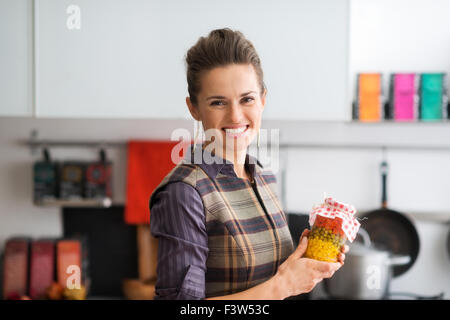 Eine glückliche, stolze Frau lächelt, als sie ein Glas frisch konserviert Herbst Gemüse in ihrer Küche hält. Stockfoto