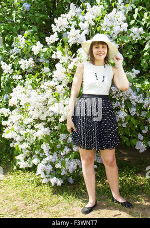 Europäischen Dame im weißen Hut stehen in der Nähe von großen Flieder Strauch in voller Blüte. Stockfoto