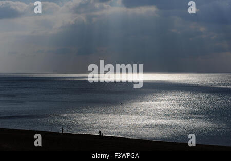 Brighton, UK. 13. Oktober 2015. Ein Mann schiebt sein Fahrrad am Strand entlang, wie die dunklen Wolken Sonnenstrahlen durchbrechen die aus Brighton heute bilden das Wetter in den nächsten Tagen Kredit mehr verunsichert werden soll: Simon Dack/Alamy Live News Stockfoto