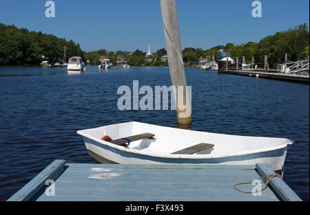 Eine weiße Jolle schwimmende am Ende ein Dock mit Booten und der fernen Stadt von Ellsworth, Maine im Sommer. Stockfoto