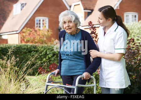 Pflegeperson Senior Menschen helfen, zu wandeln im Garten unter Verwendung des Rahmens zu Fuß Stockfoto