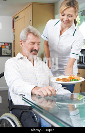 Pflegeperson servieren Mahlzeit Mann im Rollstuhl zu Hause Stockfoto