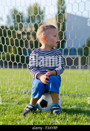 Kleiner Junge sitzt auf einem Fußball Stockfoto