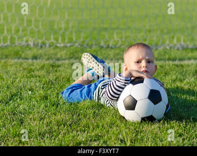 Junge mit Fußball auf dem Rasen liegend Stockfoto