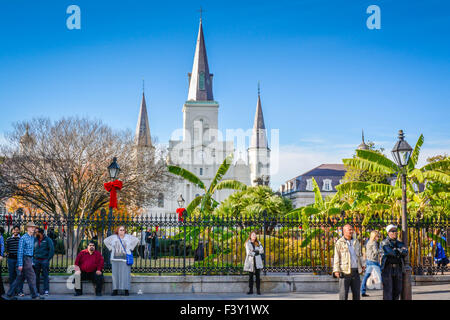 Schwarzer gusseiserner Zaun mit Menschen und roten Feiertagsbögen vor entfernten Türmen der St. Louis Cathedral am Jackson Square, New Orleans, LA Stockfoto