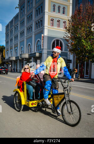 Touristen, feiert die Feiertage genießen eine Rikscha fahren durch eine Weihnachtsmütze tragen Fahrer im French Quarter in New Orleans, LA Stockfoto