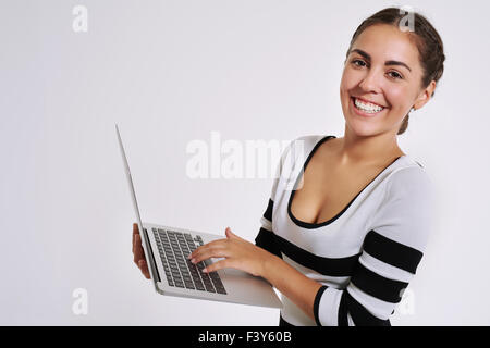 Glücklich lächelnde junge Frau mit einem handheld Laptopcomputer zum Surfen im Internet in die Kamera schaut, mit einem warmen freundlichen smi Stockfoto