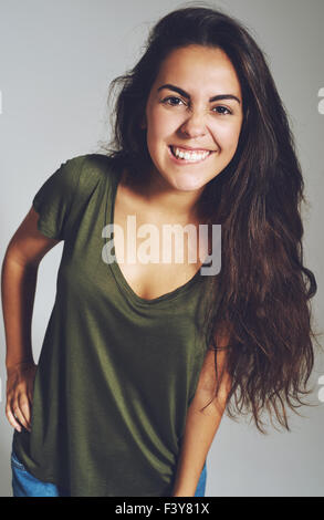 Niedliche lässige junge Frau in ein t-Shirt mit lange brünette Haare, lehnt sich nach vorne, mit einem wunderschönen Lächeln in die Kamera schaut Stockfoto