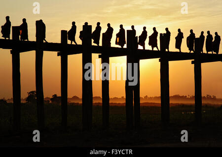 Buddhistische Mönche überquert die U Bein Brücke während des Sonnenuntergangs in Amarapura, Mandalay Region, Myanmar Stockfoto