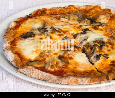 Auf dem Bild ein Stück Pizza mit Tomaten Mozzarella und Champignons auf einem weißen Teller im Restaurant serviert. Stockfoto