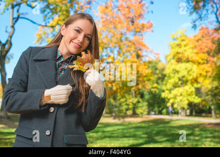 Blonde Frau im grauen Mantel hält trockene Blätter Stockfoto