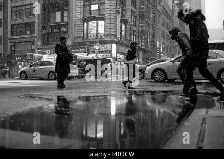 New York, New York.  20. März 2015.  Zwei Männer versuchen, über eine Pfütze von Schnee und Wasser am ersten Tag des Frühlings zu springen. Stockfoto